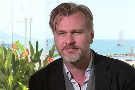 a man wearing a black jacket and white shirt sitting in front of a window looking at the camera