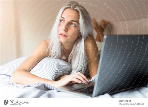 Young woman lying in bed using laptop - a Royalty Free Stock Photo from Photocase