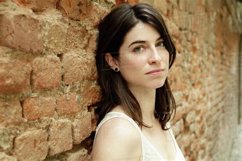 Portrait of beautiful Italian woman leaning against brick wall, Milan ...