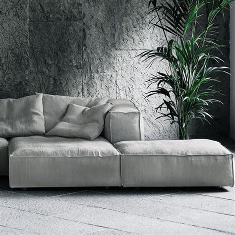 a white couch sitting next to a tall plant in a room with concrete walls and flooring