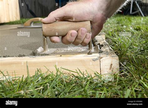 A close up of a man using a concrete edging tool on wet cement slab with timber form work in a ...