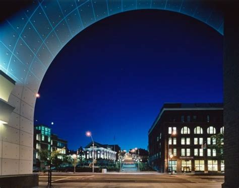 an arch is lit up at night with buildings in the background