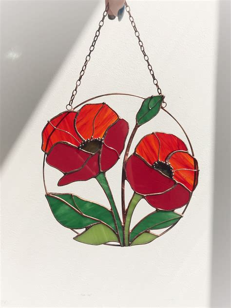 a stained glass hanging decoration with two red flowers on it's center and green leaves