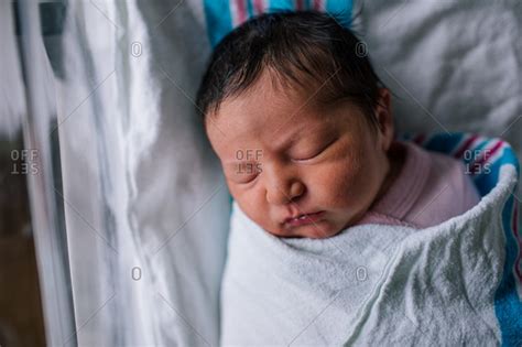 Newborn baby with thick dark hair swaddled in hospital bed stock photo - OFFSET