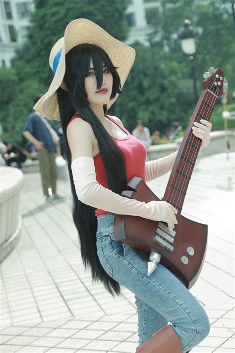 a woman with long black hair is holding a guitar and posing for the camera while wearing a straw hat