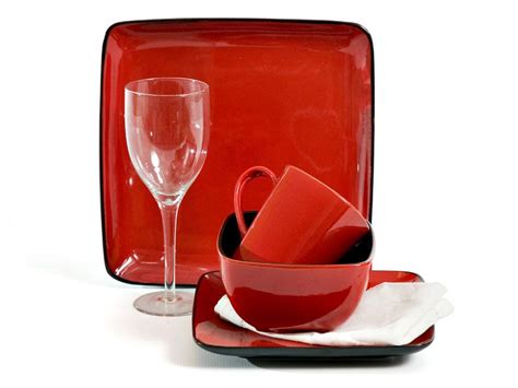 a red dinnerware set on a white background with wine glasses and napkins in the foreground