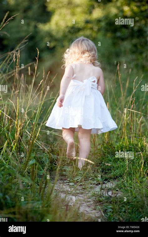 little girl in white dress walking up the way among green grass back view Stock Photo - Alamy