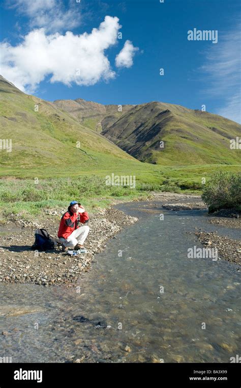 Man fills his water bottle while hiking along Chandalar River in the Brooks Range during Summer ...