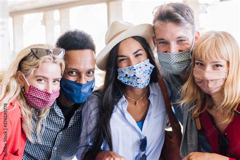 Portrait group of young happy friends wearing face mask during Covid pandemic smiling at the ...