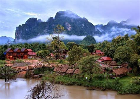 a village in the middle of a river with mountains in the background and ...