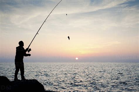 Silhouette of man fishing at sunset stock photo