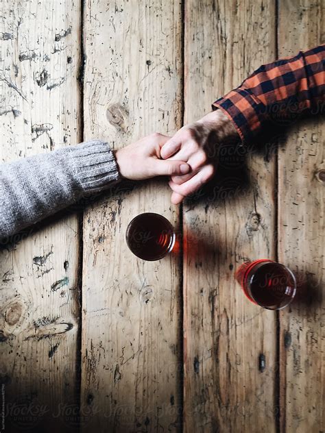 "Man And Woman Holding Hands With Two Beers On A Wooden Table" by ...