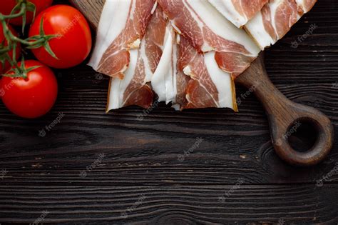 Premium Photo | Parma ham slices on dark wooden background with tomato top view flat lay