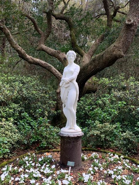 a white statue sitting in the middle of a garden