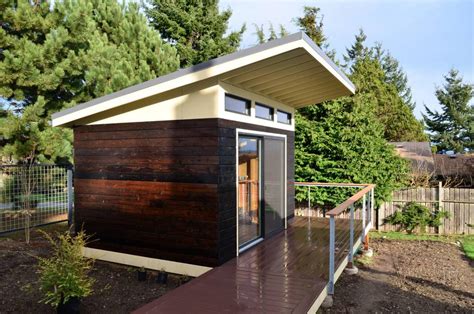 a small wooden house sitting on top of a lush green field next to a forest