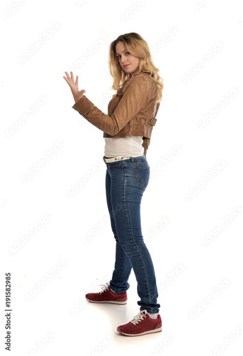 full length portrait of blonde girl wearing simple brown jacket and jeans, standing pose on ...