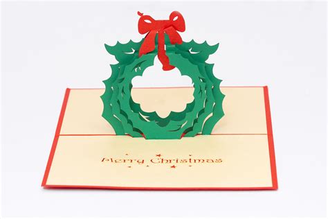 a pop up christmas card with a green wreath and red bow on it's front