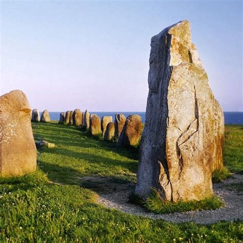 several large rocks sitting on top of a lush green field next to the ocean with blue skies in ...