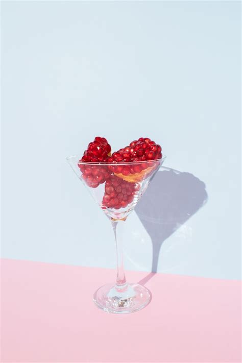 Slices of red pomegranate fruit in coctail glass with sunlight shadow ...