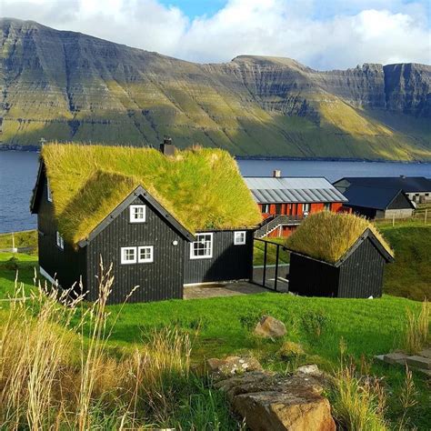 two black houses with grass roofs and mountains in the background