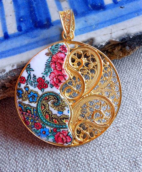 an ornately decorated pendant hangs from a blue and white tile background with red flowers