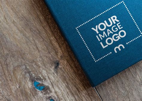 Logo Mockup Placed on Blue Book on Wooden Table - Mediamodifier