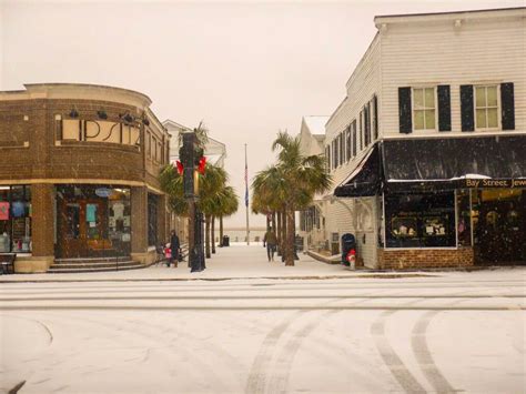 a snowy street with shops and palm trees on the corner in front of it,