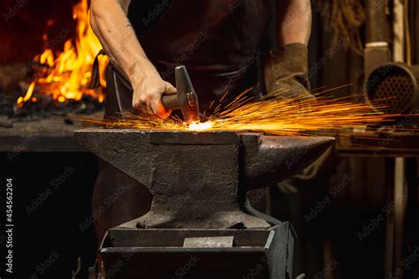 Close-up working powerful hands of male blacksmith forge an iron product in a blacksmith. Hammer ...