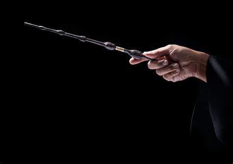 Close-up of magician's hand holding magic wand against black background ...