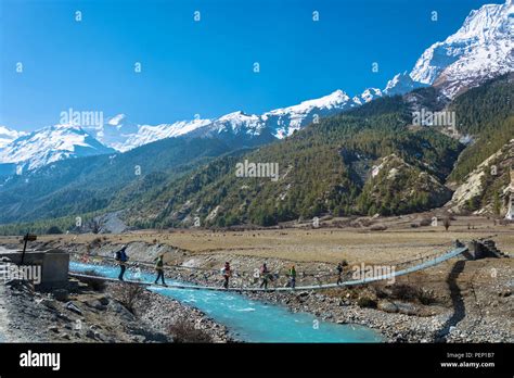 Manang, Nepal-April 3, 2018: a group of tourists is walking on a suspension bridge towards the ...