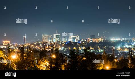 A panoramic view of Kigali city skyline lit up at night, under a deep blue evening sky with the ...