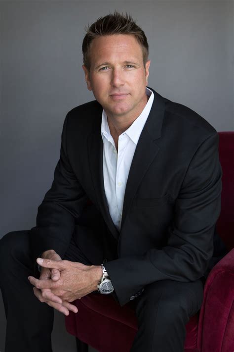 a man in a black suit and white shirt sitting on a red chair with his arms crossed