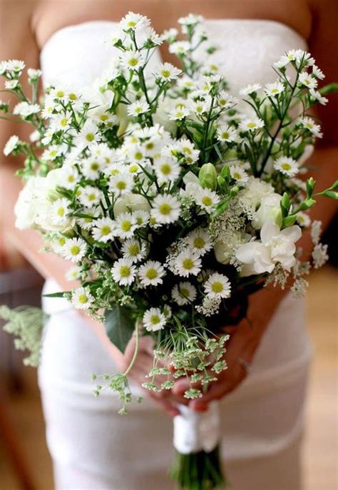 a woman holding a bouquet of white flowers in her hands and wearing a wedding dress