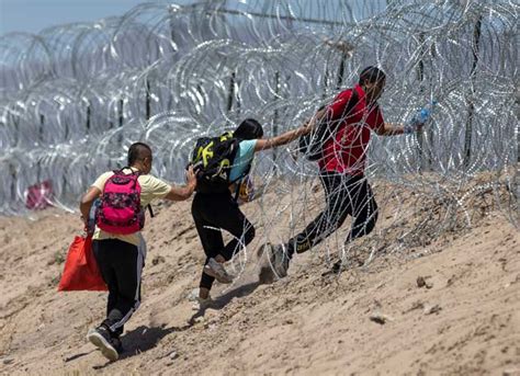 EL PASO, TEXAS - MAY 11: Immigrants walk through razor wire surrounding ...