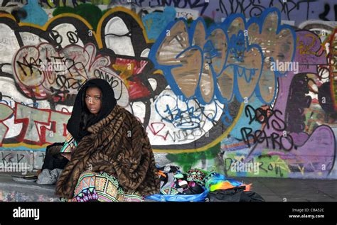 Black girl with hood sitting by a wall full of graffiti wearing a coat ...