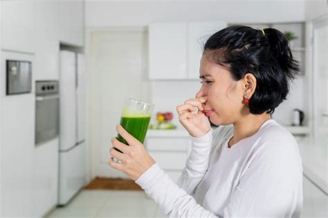 Premium Photo | Woman closing nose while holding healthy drink in kitchen