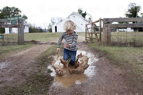 Image of Young boy splashing in muddy puddle on the farm - Austockphoto