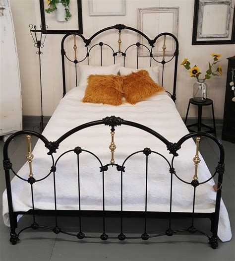 a black iron bed with white sheets and orange pillows on it's headboard