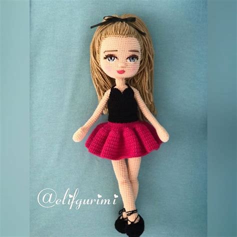 a crocheted doll is hanging on a blue wall with a black top and pink skirt