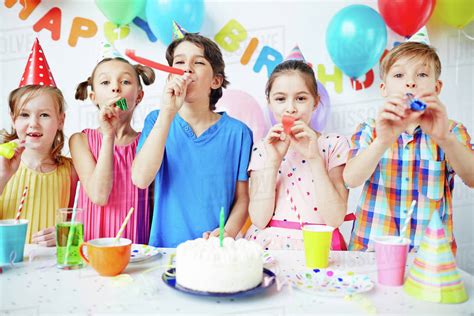 Row of happy kids blowing horns at birthday party - Stock Photo - Dissolve