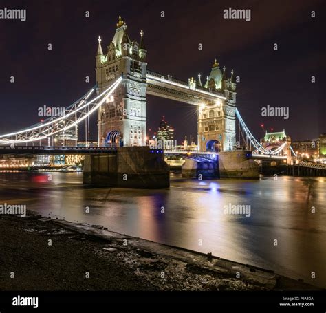 View of Tower Bridge lit up at night from the banks of the River Thames, London, with the ...