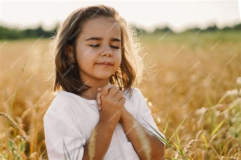 Premium Photo | Little girl closed her eyes, praying in a field wheat. hands folded in prayer ...