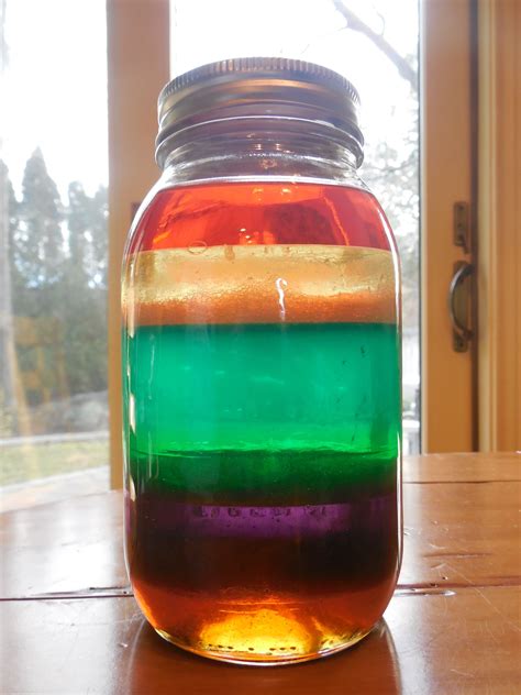 a jar filled with liquid sitting on top of a wooden table next to a window