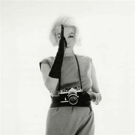 a woman holding a camera in her right hand and wearing a dress with an attached belt