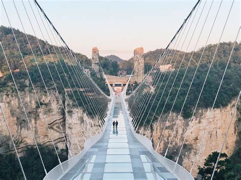 two people walking across a suspension bridge with mountains in the background