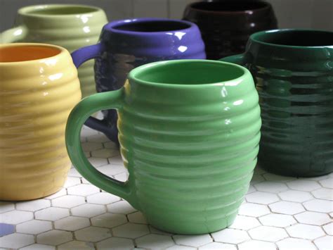 several different colored coffee mugs sitting on a tiled counter top, all lined up