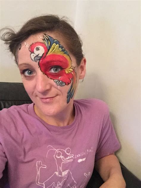 a woman with her face painted like a bird on her cheek and the image of a parrot on her forehead