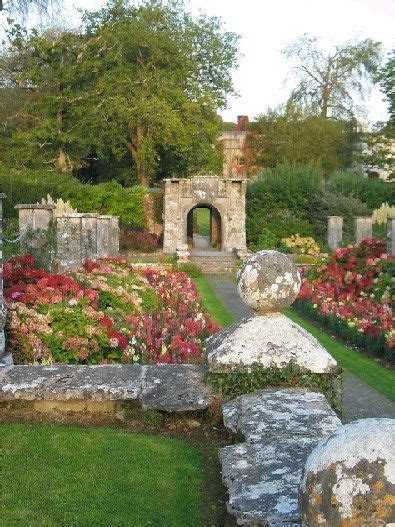 the garden is full of colorful flowers and stone structures, with an archway in the middle