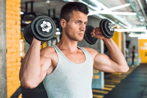 Young man doing exercise with dumbbells for strengthening his shoulder Photo | Free Download