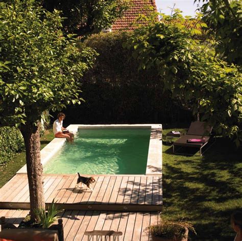 a man sitting on the edge of a swimming pool next to a tree and lawn